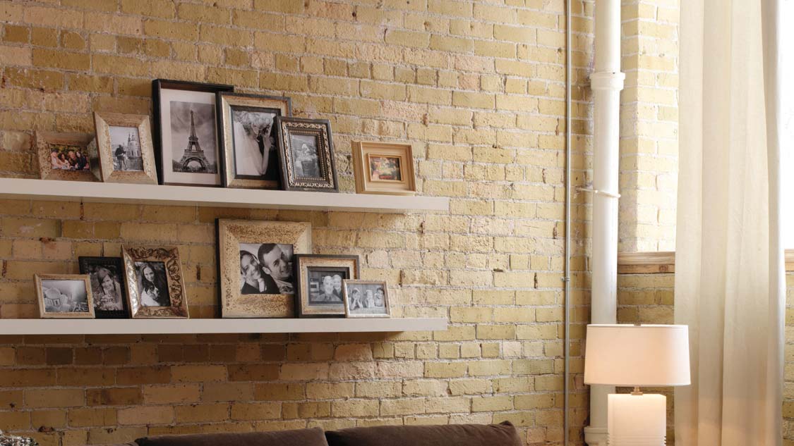 Various picture frames on white shelves against a cream-colored brick wall